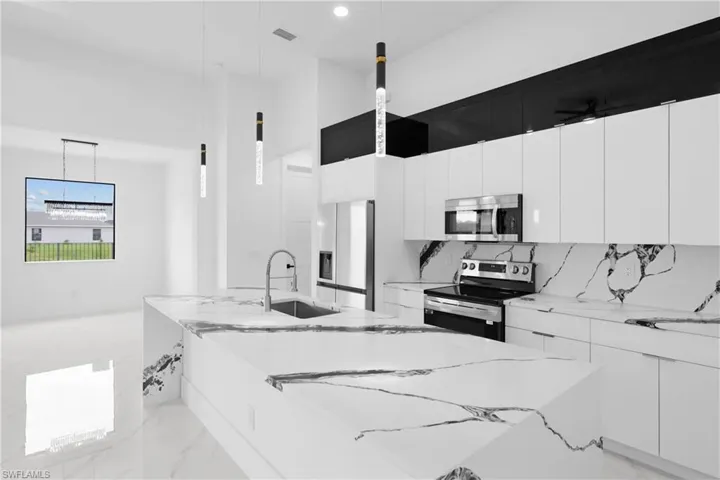 Kitchen with white cabinets, hanging light fixtures, light stone countertops, and stainless steel appliances