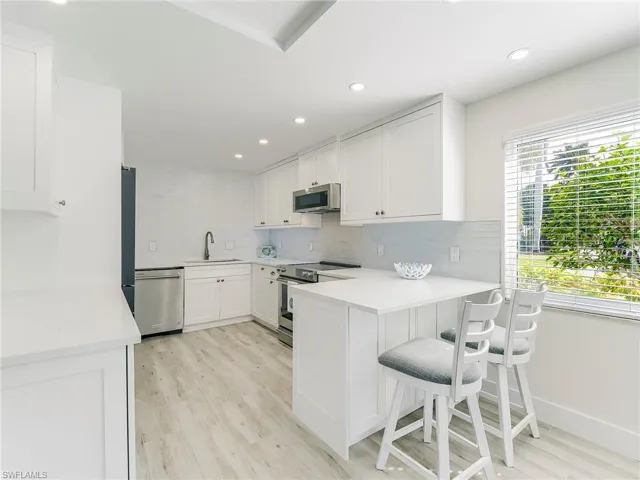 Kitchen featuring white cabinetry, backsplash, a breakfast bar, stainless steel appliances, and recessed lighting