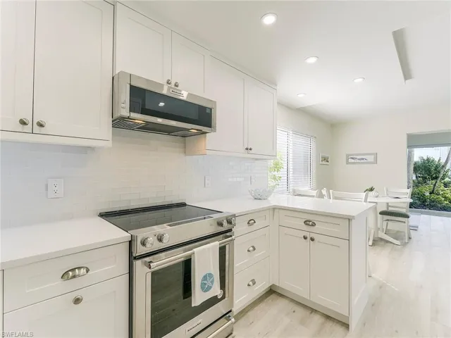 Kitchen with stainless steel appliances, white cabinetry, a peninsula, light wood finished floors, and recessed lighting