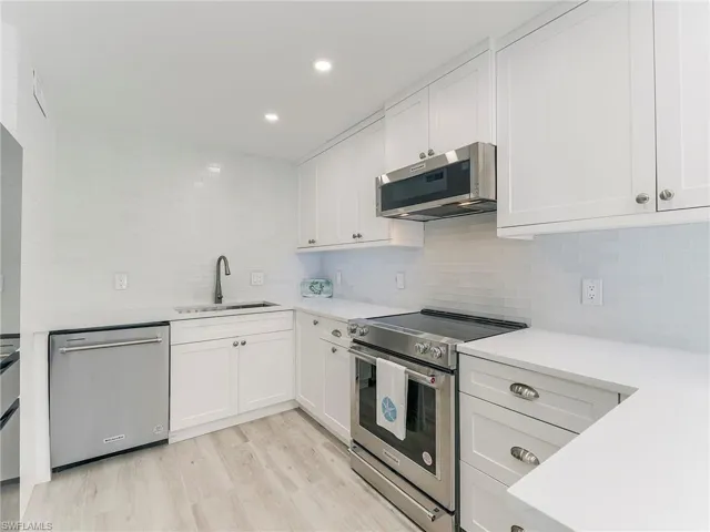 Kitchen with stainless steel appliances, white cabinetry, light wood-type flooring, tasteful backsplash, and recessed lighting