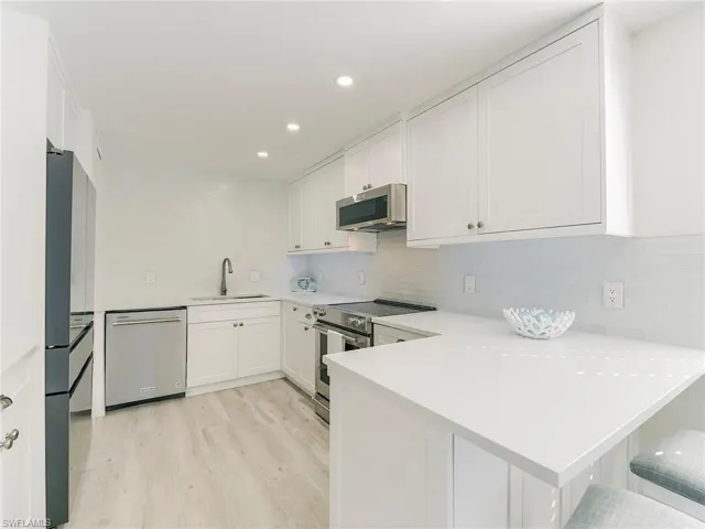Kitchen featuring a peninsula, stainless steel appliances, white cabinets, a kitchen breakfast bar, and recessed lighting