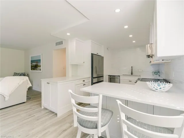 Kitchen with a peninsula, backsplash, white cabinets, a kitchen breakfast bar, and recessed lighting