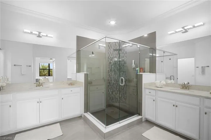 Expansive bathroom featuring a central glass-enclosed shower, dual vanity sinks, extensive counter space, white cabinetry, and large wall-mounted mirrors