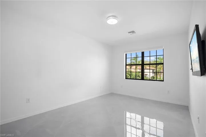 Spacious room featuring light gray tile flooring, crisp white walls, and a large window with black grilles