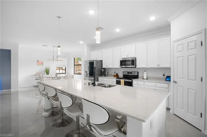 Expansive kitchen island featuring a light-toned countertop, stainless steel double basin sink, and pendant lighting