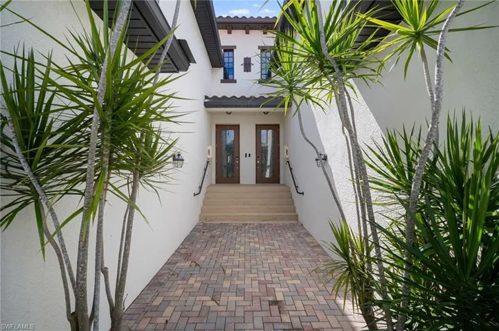 Inviting entryway featuring a paver walkway, stucco exterior, and dual glass-paneled wooden doors