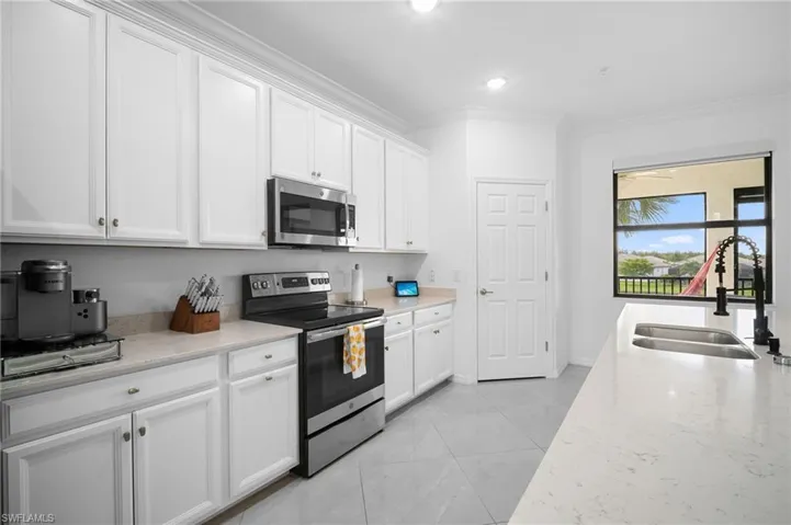 Contemporary kitchen featuring white cabinetry, light-toned countertops, stainless steel appliances, and a double basin sink with a black high-arc faucet