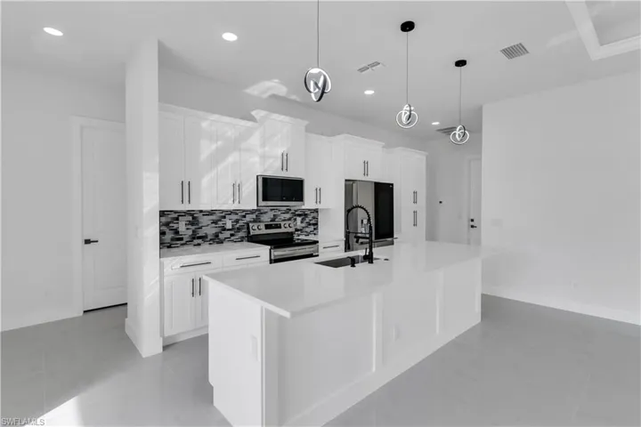 Kitchen with stainless steel appliances, a sink, visible vents, decorative backsplash, and an island with sink