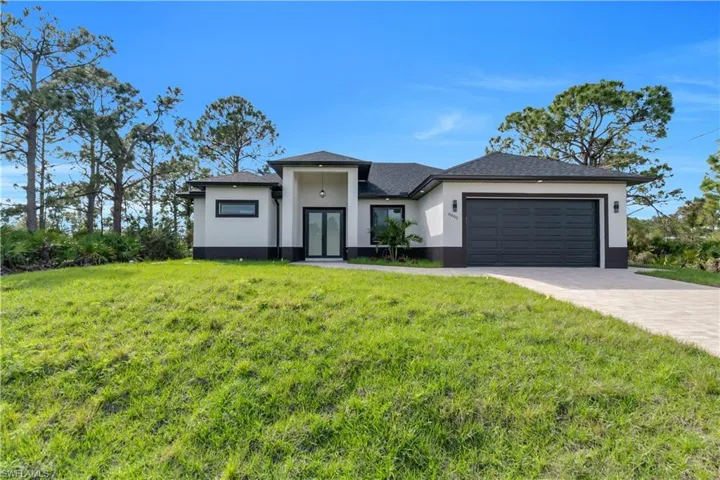 Prairie-style house with a front lawn, decorative driveway, an attached garage, and stucco siding