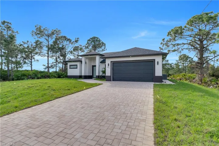 Prairie-style home featuring an attached garage, stucco siding, decorative driveway, and a front yard