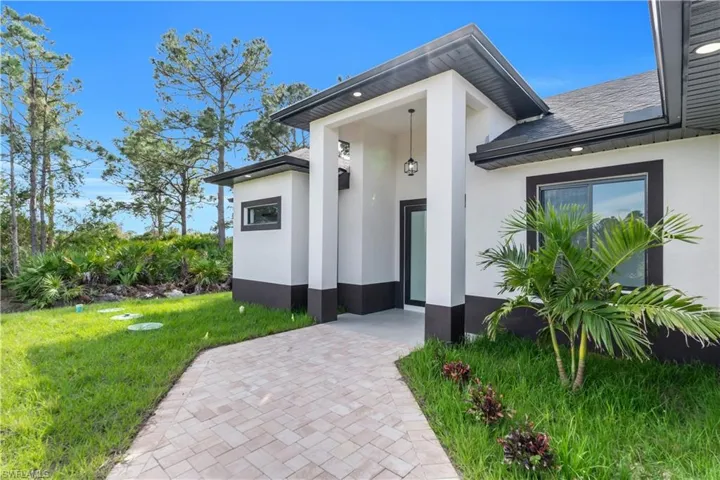 Property entrance featuring roof with shingles, a yard, and stucco siding