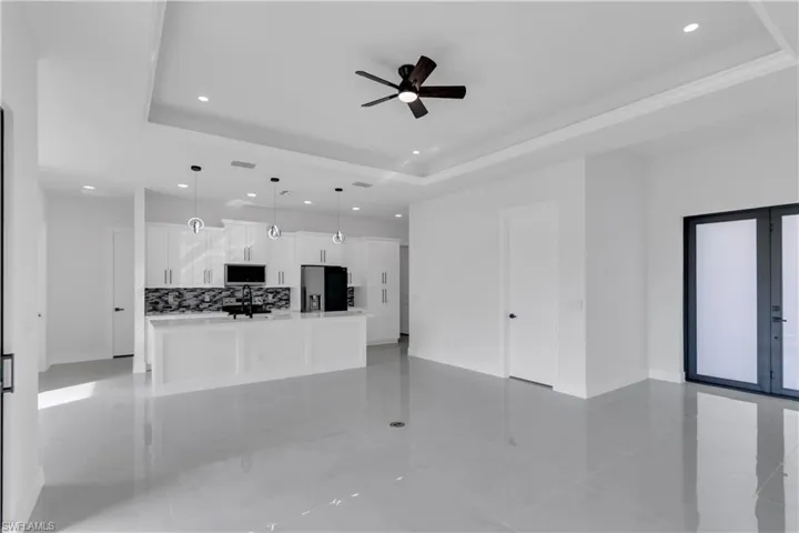 Unfurnished living room with baseboards, a raised ceiling, ceiling fan, french doors, and recessed lighting