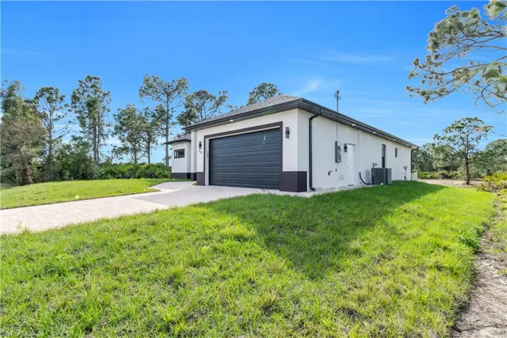 View of side of home with stucco siding, a lawn, an attached garage, cooling unit, and driveway