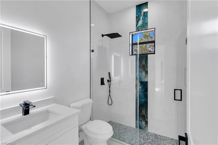 Bathroom with toilet, vanity, and a marble finish shower
