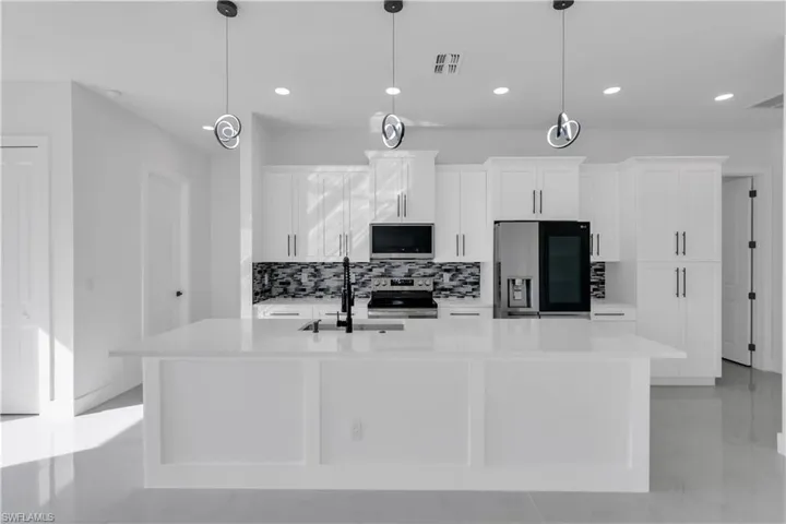 Kitchen with stainless steel appliances, visible vents, white cabinets, a sink, and an island with sink