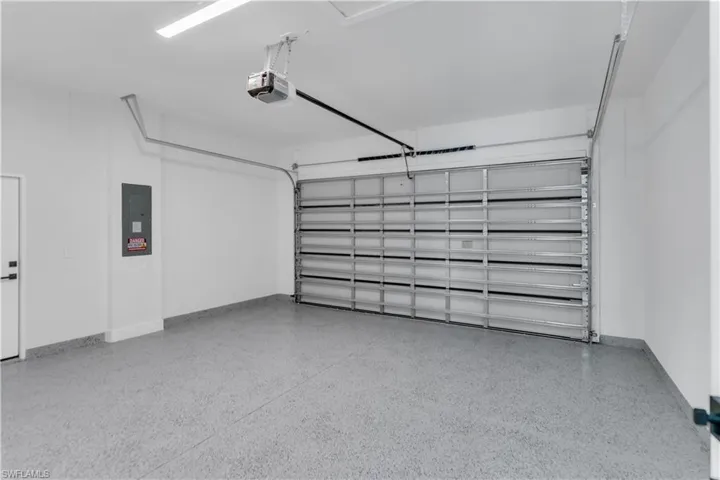 Garage featuring baseboards, electric panel, and a garage door opener