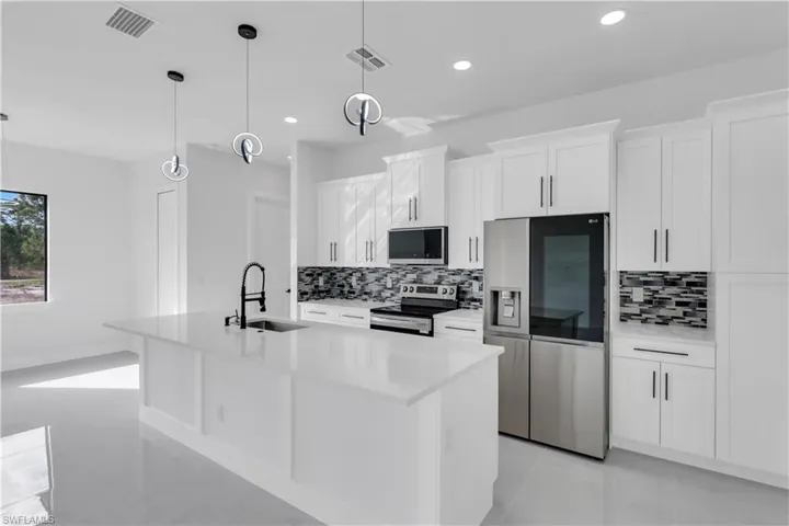 Kitchen featuring stainless steel appliances, a kitchen island with sink, visible vents, and a sink