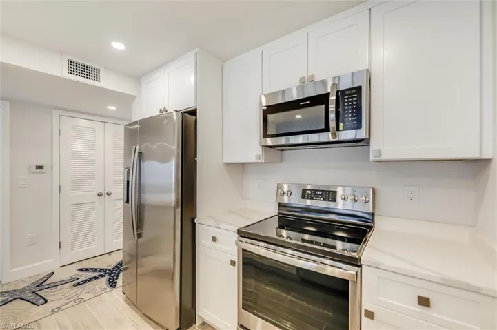 Kitchen with stainless steel appliances, white cabinetry, recessed lighting, and light stone counters