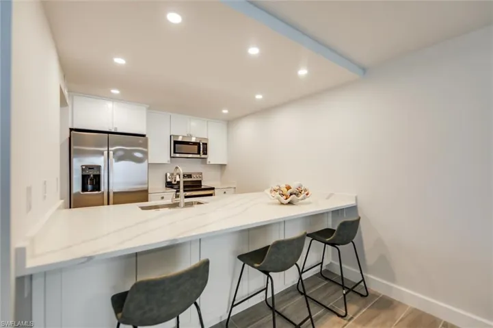 Kitchen featuring a peninsula, appliances with stainless steel finishes, recessed lighting, light stone counters, and white cabinets