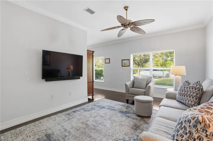 Living room with ornamental molding, a ceiling fan, and dark wood-style floors
