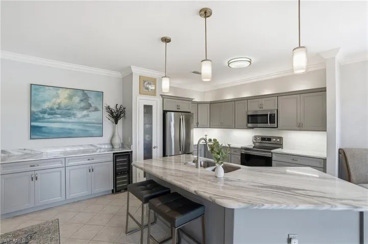 Kitchen with gray cabinetry, stainless steel appliances, a kitchen breakfast bar, decorative light fixtures, and backsplash