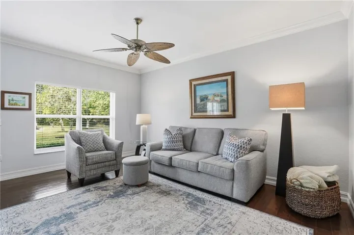Living room featuring ornamental molding, dark wood-style flooring, and ceiling fan