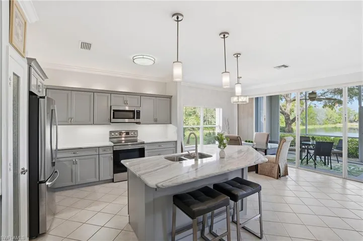 Kitchen with gray cabinetry, stainless steel appliances, a kitchen breakfast bar, pendant lighting, and ornamental molding