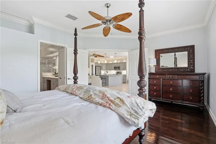 Bedroom with ornamental molding, dark wood-style floors, a ceiling fan, ensuite bath, and freestanding refrigerator