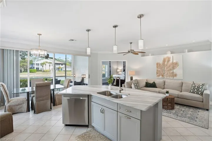 Kitchen featuring open floor plan, light stone counters, decorative light fixtures, stainless steel dishwasher, and ornamental molding