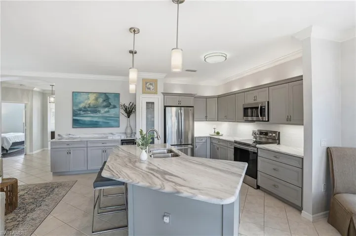 Kitchen featuring gray cabinetry, stainless steel appliances, a kitchen bar, crown molding, and decorative light fixtures