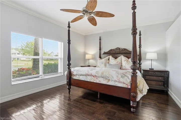 Bedroom with a ceiling fan, dark wood-style floors, and ornamental molding