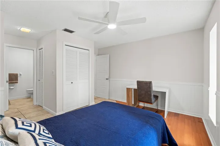 Bedroom featuring a wainscoted wall, a textured ceiling, light wood-style floors, ceiling fan, and connected bathroom