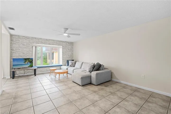 Living room with a textured ceiling, ceiling fan, and light tile patterned flooring