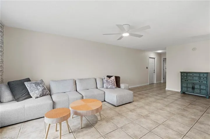 Living room with ceiling fan, light tile patterned floors, and baseboards