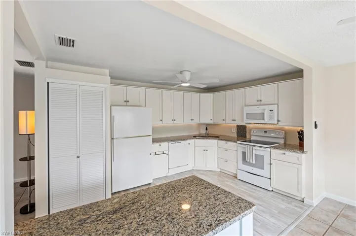 Kitchen featuring white appliances, ceiling fan, stone countertops, white cabinets, and baseboards
