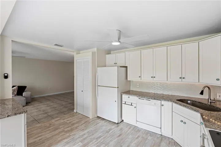 Kitchen featuring white appliances, a sink, ceiling fan, white cabinets, and stone counters