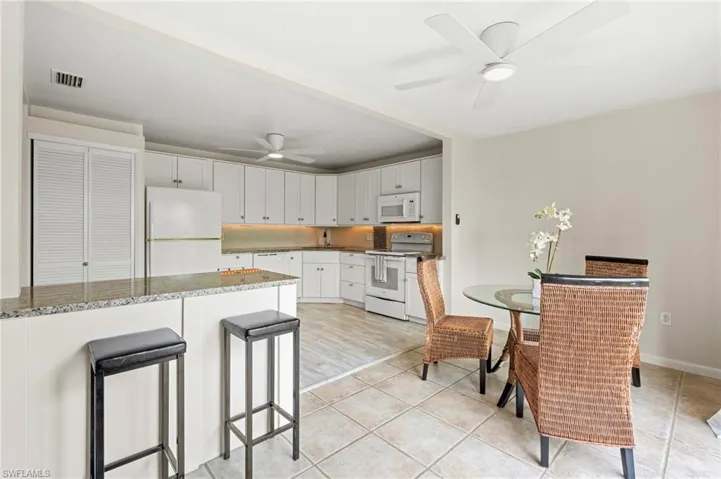 Kitchen featuring white appliances, ceiling fan, white cabinetry, light tile patterned flooring, and a breakfast bar area