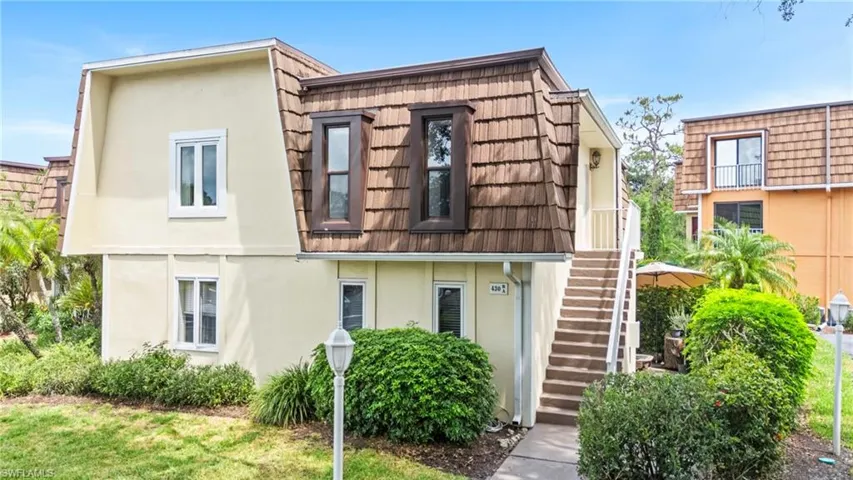 View of front of property with stairway, stucco siding, and mansard roof