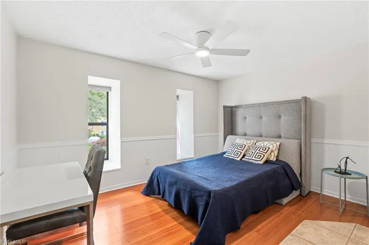Bedroom with wood finished floors, a textured ceiling, ceiling fan, and wainscoting