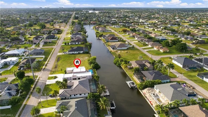 Aerial perspective of a waterfront property featuring direct canal access, a private swimming pool, and concrete hardscaping