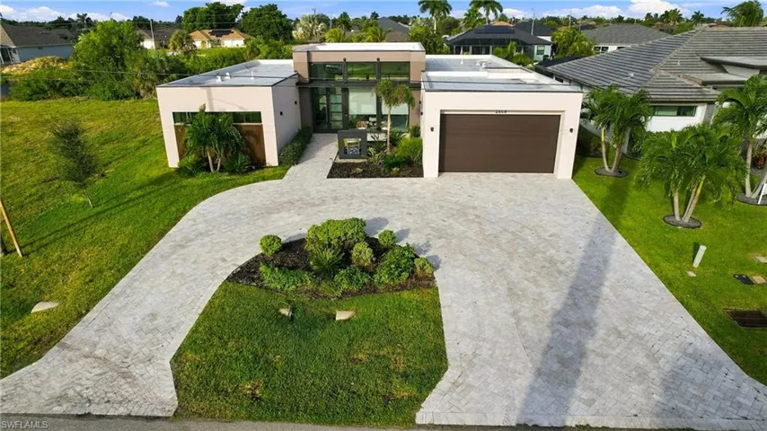 Contemporary single-story residence featuring a flat roofline, paver circular driveway, large multi-pane glass entryway, attached two-car garage, and landscaped front lawn