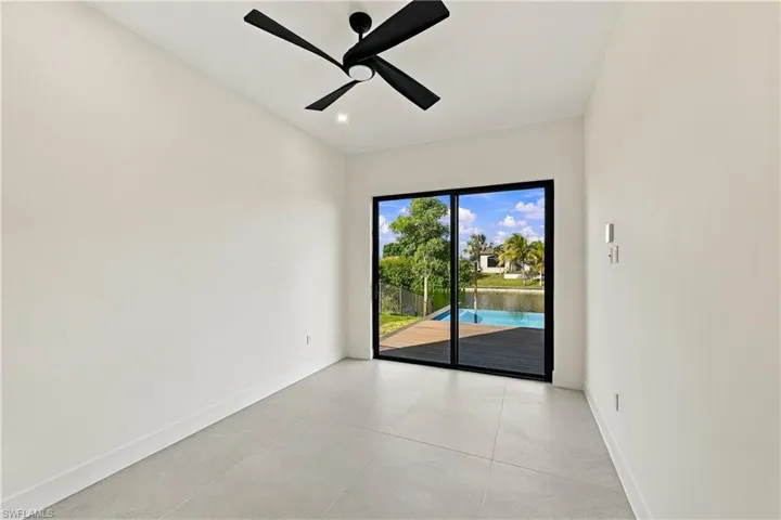 Room featuring large-format tile flooring, matte black ceiling fan, and black-framed sliding glass doors opening to a pool and water scenery