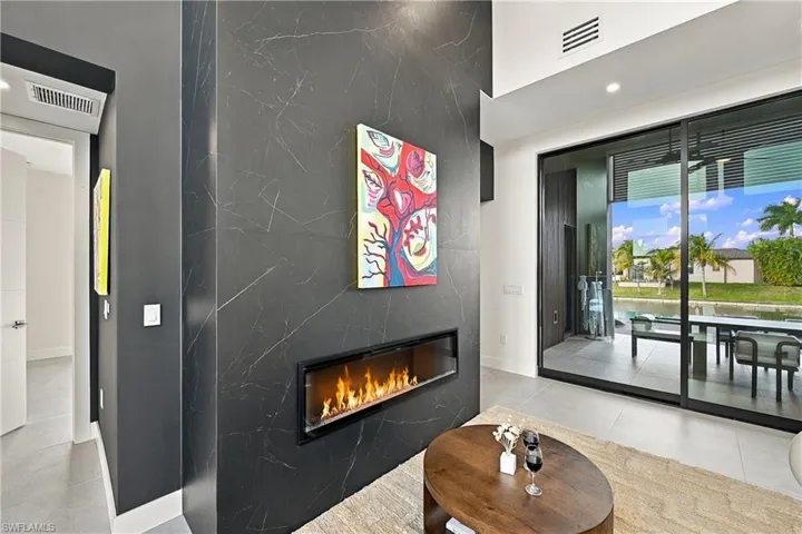 Floor-to-ceiling dark stone fireplace surround, built-in linear electric fireplace, large-format tile flooring, and oversized sliding glass doors