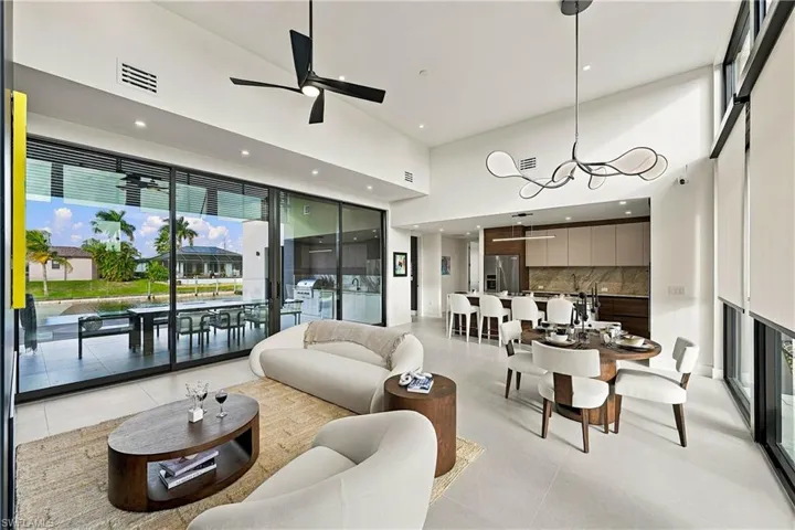 Vaulted ceilings, expansive floor-to-ceiling sliding glass doors, stone-finish kitchen backsplash, built-in cabinetry, and integrated statement lighting
