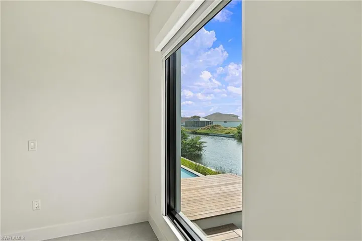 Floor-to-ceiling black-framed window featuring exterior water frontage, wood-finish decking, and built-in shade housing