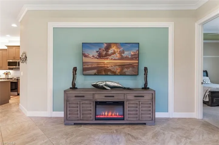 Detailed view of crown molding, stainless steel appliances, recessed lighting, and a glass covered fireplace