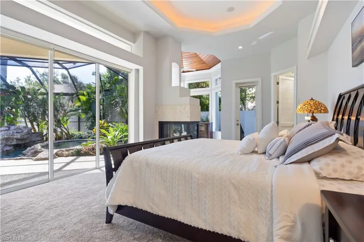Carpeted bedroom with access to exterior, a raised ceiling, a multi sided fireplace, and a sunroom