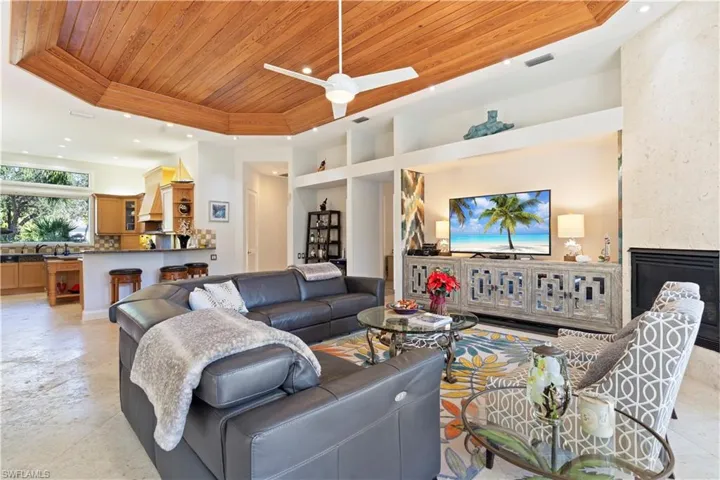 Living room with a raised ceiling, wooden ceiling, a fireplace, recessed lighting, and ceiling fan