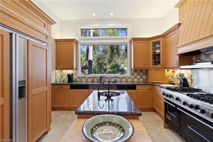 Kitchen featuring high end appliances, brown cabinets, premium range hood, and recessed lighting