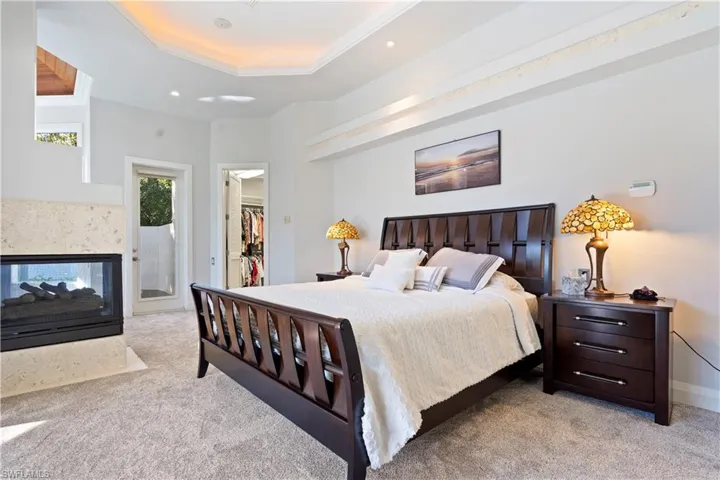 Bedroom with a multi sided fireplace, a walk in closet, a tray ceiling, light carpet, and recessed lighting